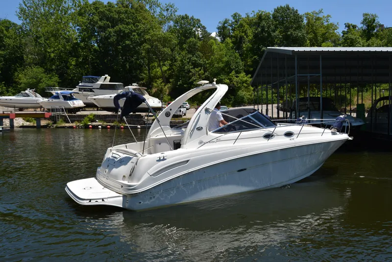 Slide: The Image of 2004 Sea Ray 300 Sundancer boat docked on a sunny day, surrounded by trees and other boats. - 3