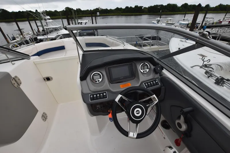 Slide: The Image of 2018 Chaparral 230 Suncoast boat dashboard with steering wheel and control panel, docked by the water. - 9