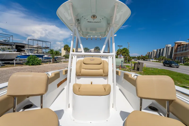 Slide: The Image of 2017 Sea Hunt Ultra 225 boat interior with beige seating, parked near a marina under a clear blue sky. - 12