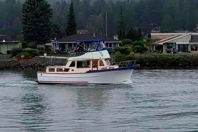 The Image of 1979 Transpac Eagle 36 Trawler cruising near waterfront homes on a cloudy day. - 0