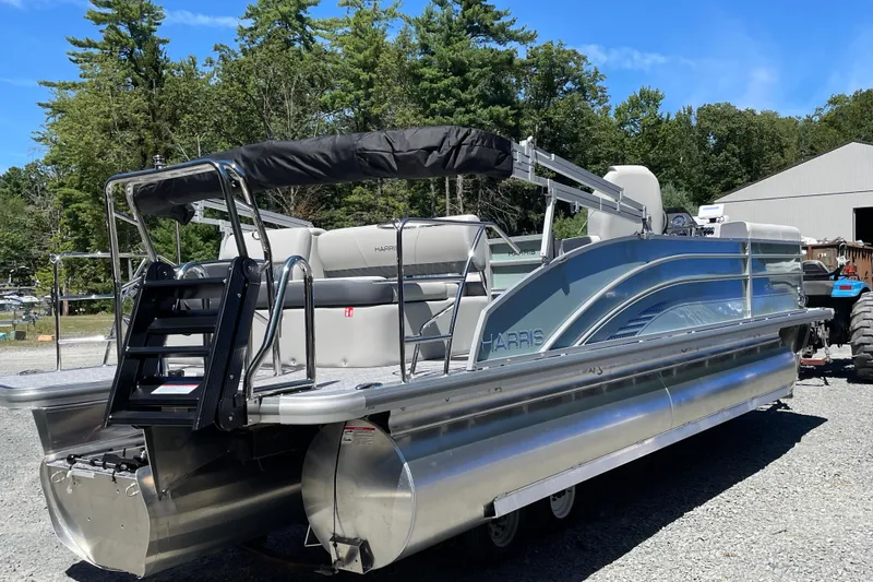 The Image of 2026 Harris Cruiser 230 pontoon boat parked outdoors, surrounded by trees and a building. - 1