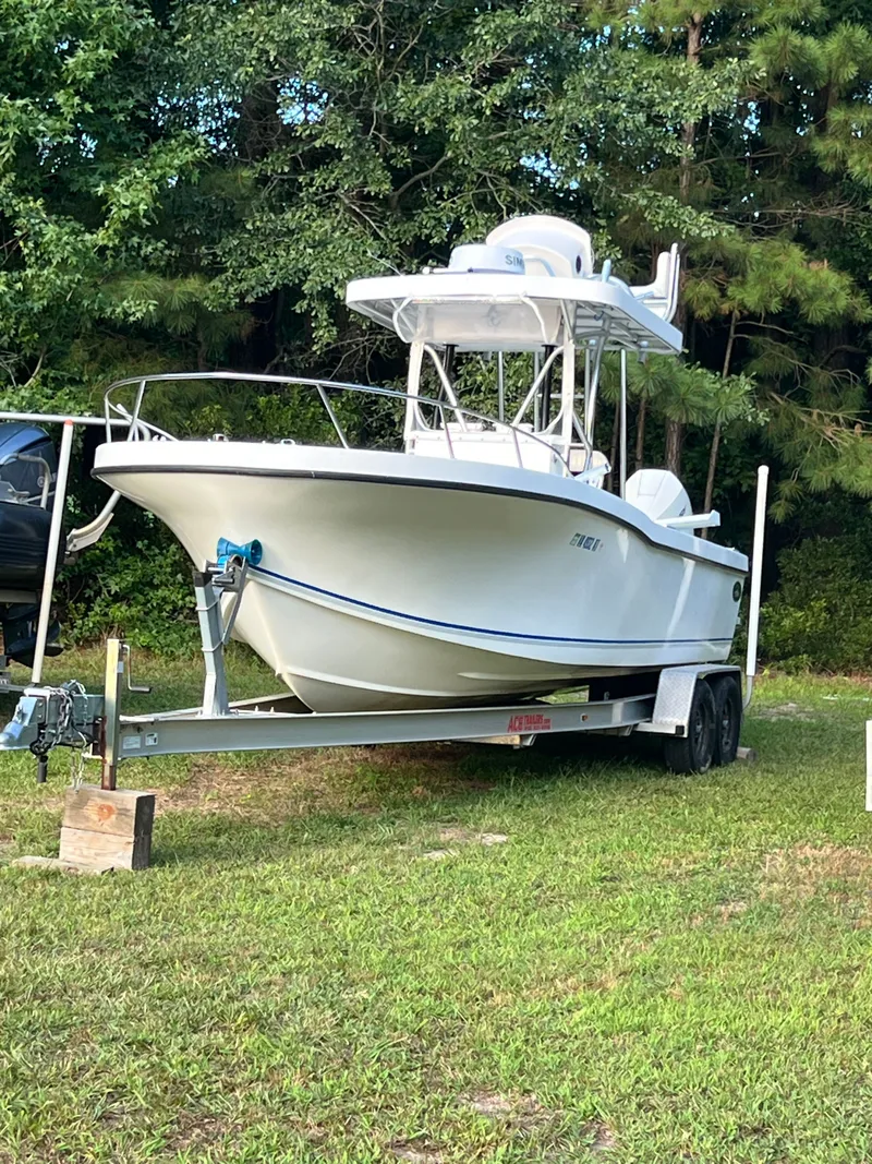 Slide: The Image of A 1998 Dusky 256 boat on a trailer, parked on grass with trees in the background. - 2