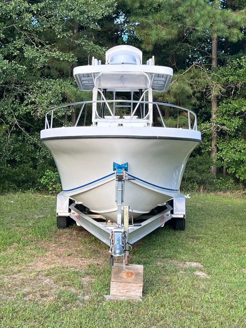 Slide: The Image of Front view of a 1998 Dusky 256 boat on a trailer, surrounded by trees. - 4
