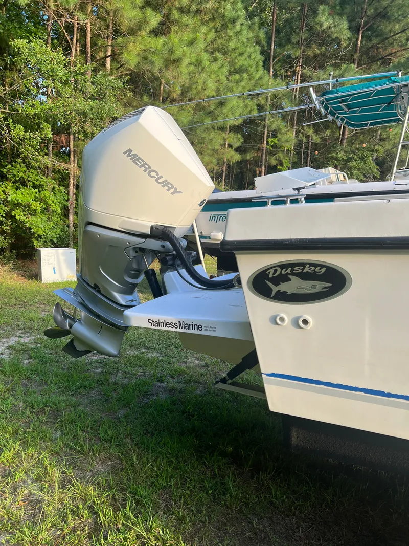 Slide: The Image of Dusky 256 boat with Mercury outboard motor, parked on grass, surrounded by trees. - 8