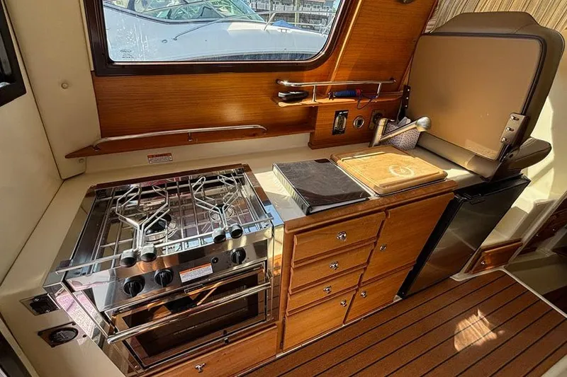 Slide: The Image of 2021 Ranger Tugs R-27 interior kitchen with stove, fridge, and wooden cabinetry. - 22