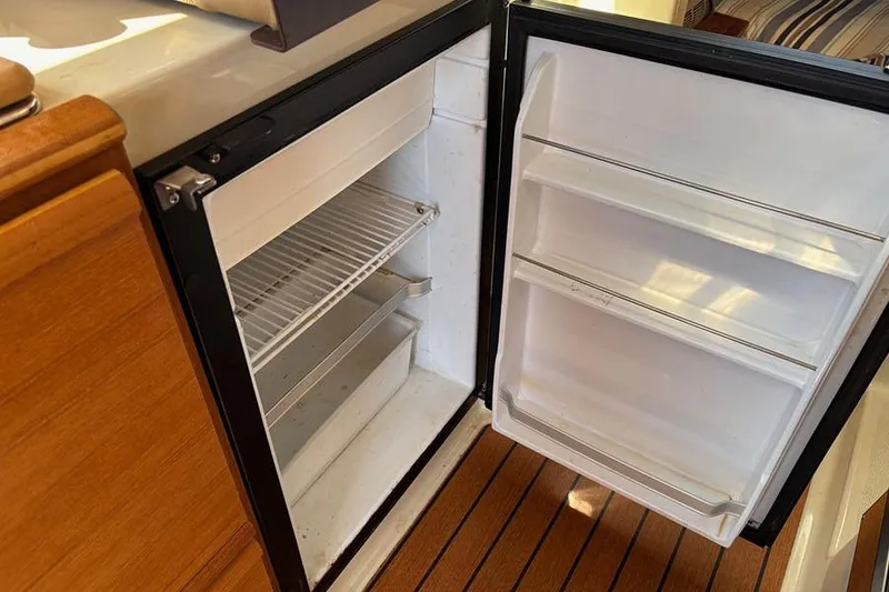 Slide: The Image of Open refrigerator inside 2021 Ranger Tugs R-27 boat, showcasing interior shelves and wooden flooring. - 27