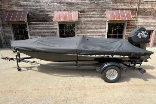 Slide: The Image of 2025 Tracker PRO170 boat covered on trailer, parked by rustic building. - 6