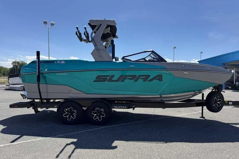 Slide: The Image of 2026 Supra SA boat on trailer, turquoise and gray design, parked outdoors. - 2