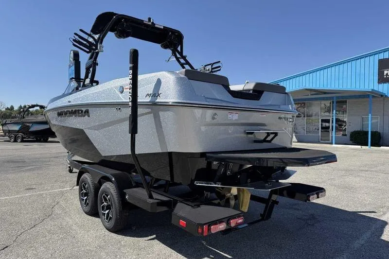 Slide: The Image of 2026 Moomba Max boat on trailer, parked outside a blue building. - 2