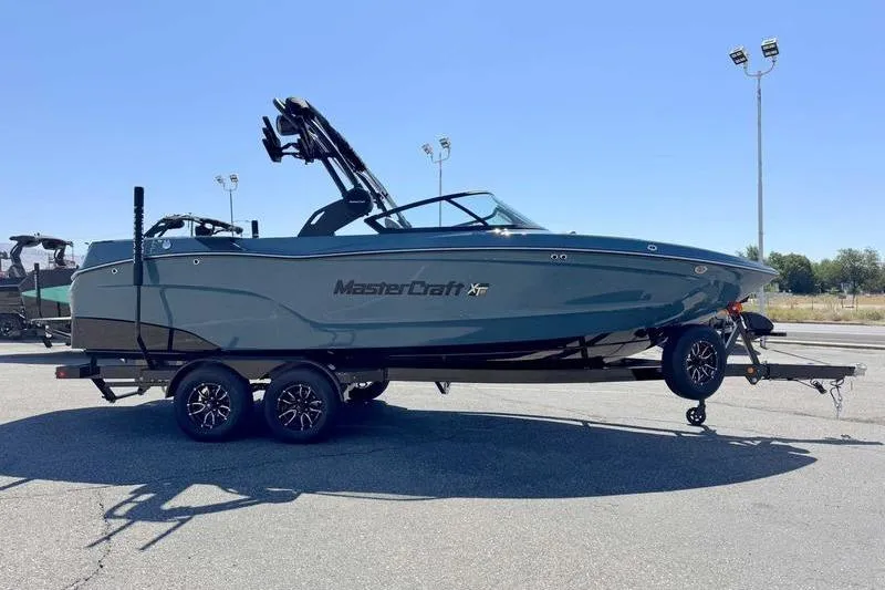 The Image of 2026 MasterCraft XT23 boat on trailer, parked outdoors under clear sky. - 1