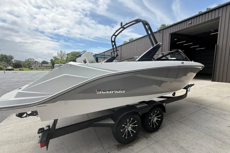 Slide: The Image of 2026 Scarab 235 SE boat on trailer, parked outside a large garage. - 2