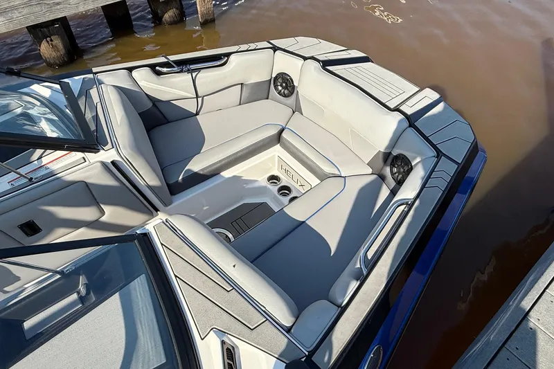 Slide: The Image of 2019 Moomba Helix boat interior with gray seating and cup holders, docked by the water. - 2