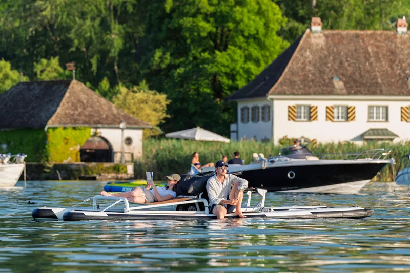 Slide: The Image of Couple relaxing on 2025 OTTER Otter Bike on a scenic lake with boats and houses. - 5