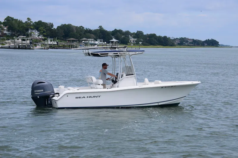 Slide: The Image of 2015 Sea Hunt Triton 210 boat cruising on calm waters with scenic shoreline background. - 2