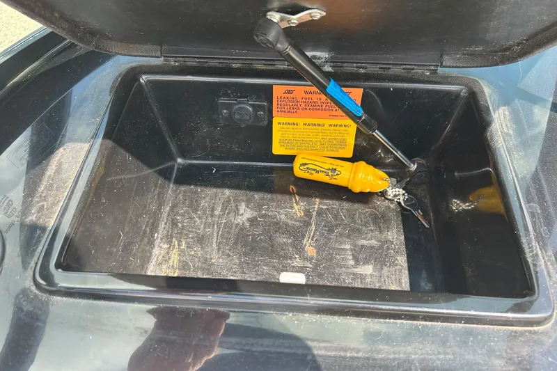 Slide: The Image of Open storage compartment in 1999 Malibu Sunsetter VLX boat with keys and warning label. - 17