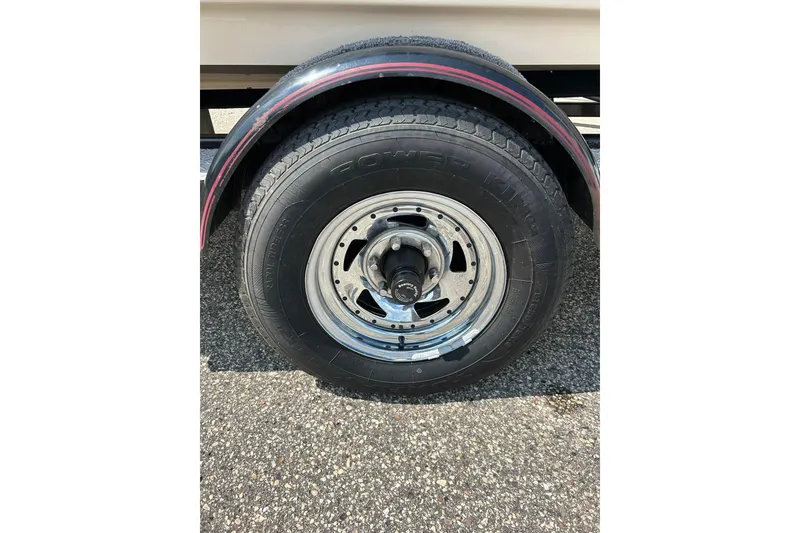 Slide: The Image of 1999 Malibu Sunsetter VLX trailer wheel with black tire on asphalt surface. - 34