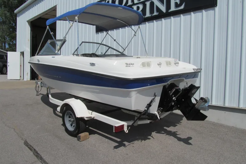 Slide: The Image of 2007 Bayliner 185 boat with blue canopy on trailer, parked outside a marine shop. - 3