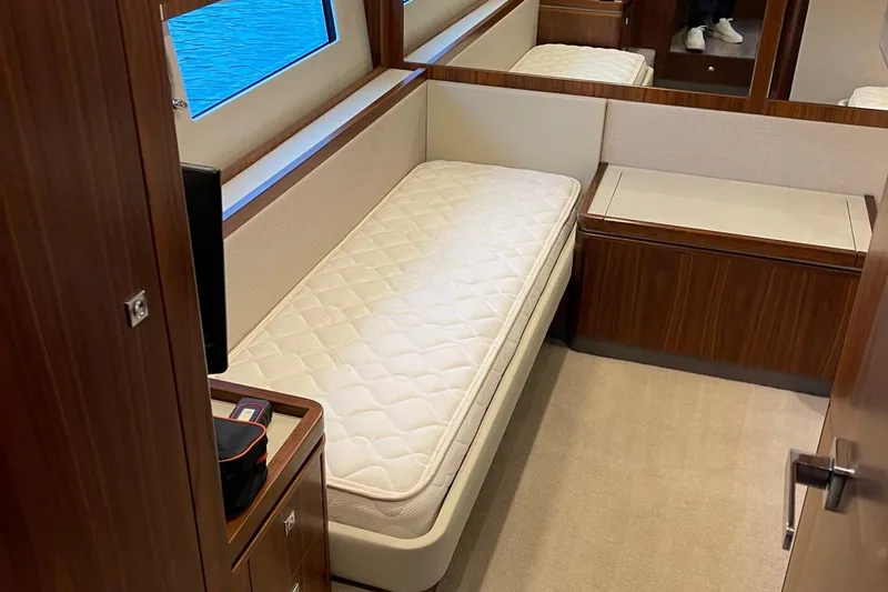 Slide: The Image of 2020 Riviera 4800 Sport Yacht interior with single bed, wooden cabinetry, and window view. - 12