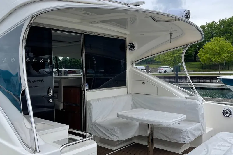 Slide: The Image of 2020 Riviera 4800 Sport Yacht with covered seating area and table, docked near greenery. - 5