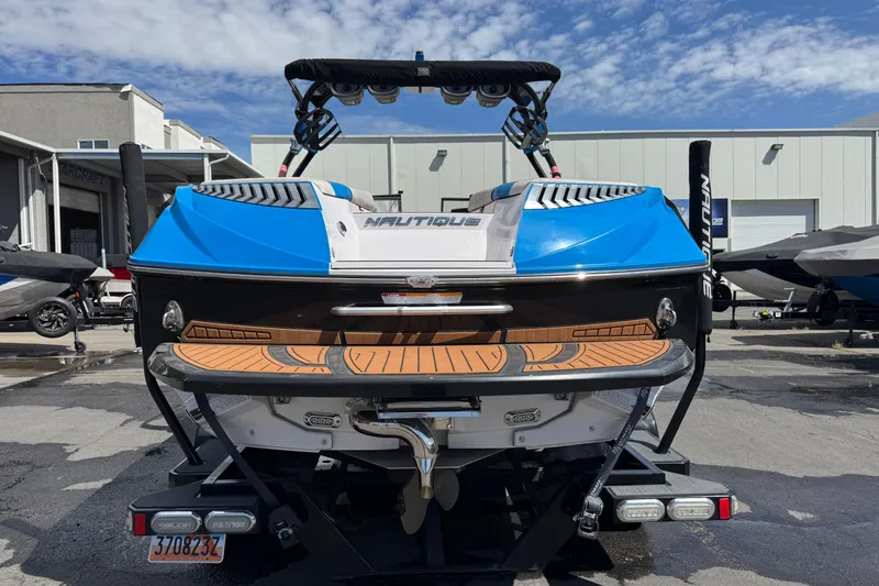 Slide: The Image of 2015 Nautique Super Air Nautique G25 boat, blue and white, rear view at a marina. - 3