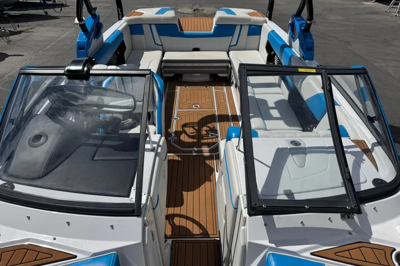 Slide: The Image of 2015 Nautique Super Air Nautique G25 interior with blue and white seating, open windshield, and wood flooring. - 8