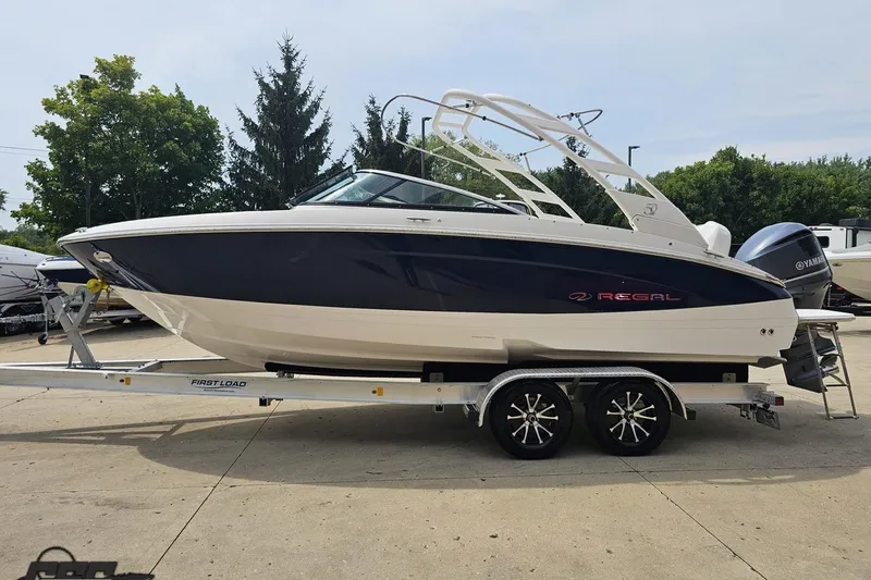 Slide: The Image of 2021 Regal LX4 boat on trailer, parked outdoors with trees in background. - 20