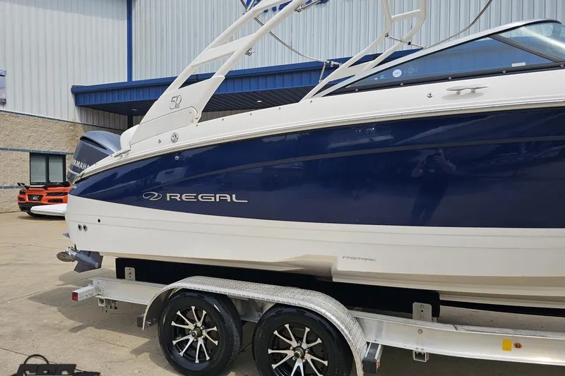 Slide: The Image of 2021 Regal LX4 boat on trailer, blue and white design, parked outside a building. - 5