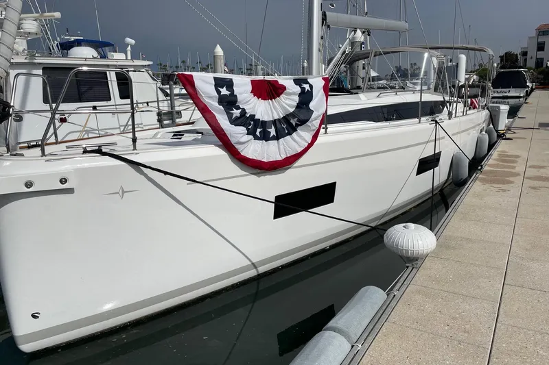 Slide: The Image of 2023 Bavaria C42 yacht docked, adorned with patriotic bunting, in a marina setting. - 1