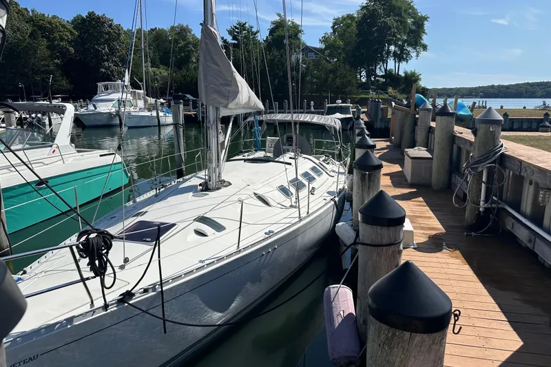 Slide: The Image of 1989 Beneteau First 41s5 sailboat docked at a marina with lush greenery. - 2