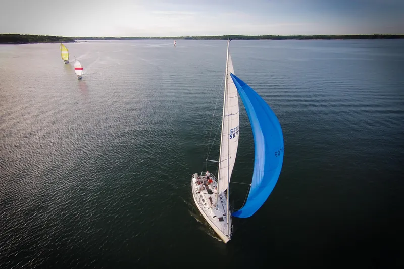 Slide: The Image of Aerial view of 1989 Beneteau First 41S5 sailboat with blue spinnaker on calm water. - 39
