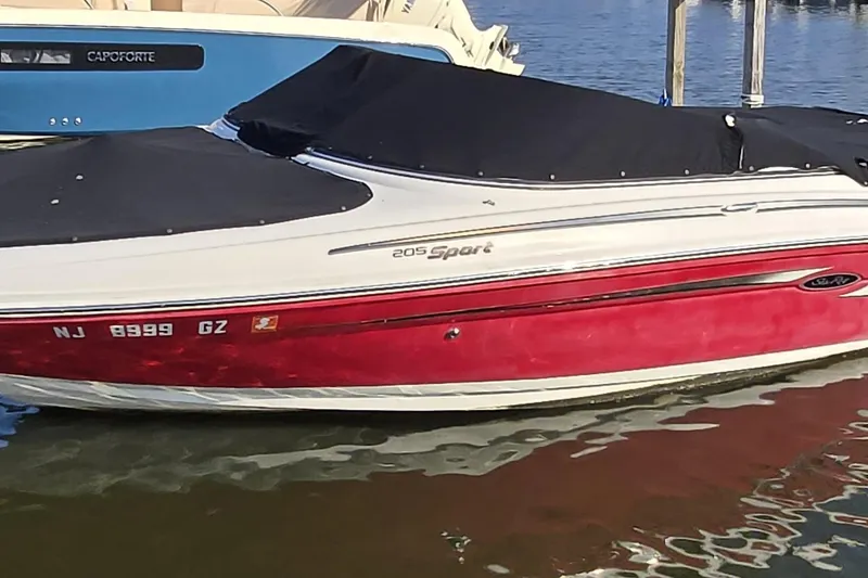 The Image of 2007 Sea Ray 205 Sport boat with red hull and black cover docked in water. - 0