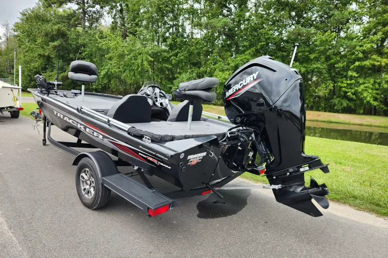 Slide: The Image of 2023 Tracker Pro Team 190 TX boat with Mercury engine on trailer, parked near greenery. - 2
