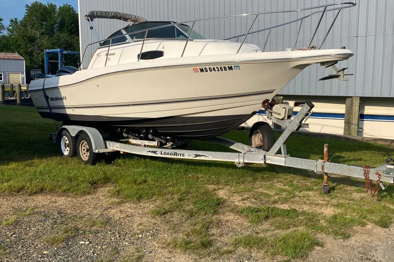 The Image of 2002 Wellcraft 24 Coastal Walkaround boat on trailer, parked on grass near a building. - 0