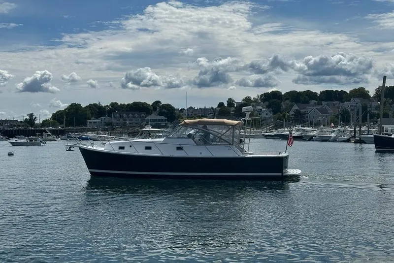 Slide: The Image of 2002 Mainship Pilot 34 cruising in a scenic harbor under a partly cloudy sky. - 2