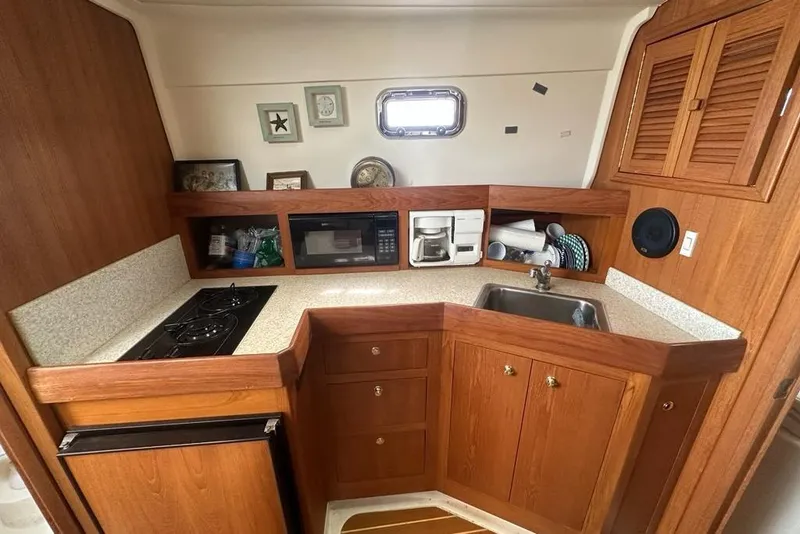 Slide: The Image of 2002 Mainship Pilot 34 galley with stove, sink, microwave, and wooden cabinetry. - 20
