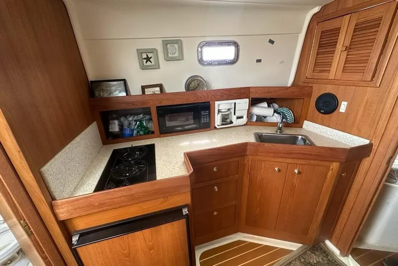 Slide: The Image of 2002 Mainship Pilot 34 galley with wood cabinetry, stove, microwave, and sink. - 21