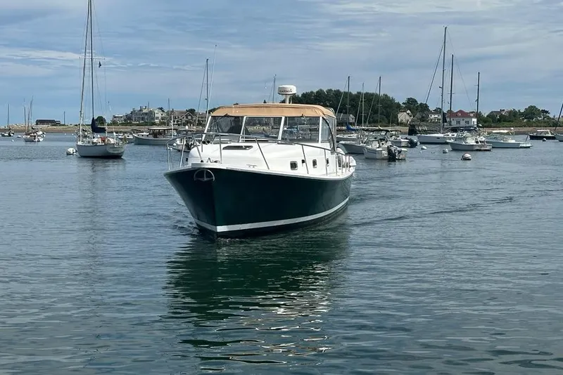 Slide: The Image of 2002 Mainship Pilot 34 cruising in a scenic harbor with sailboats and houses in the background. - 4