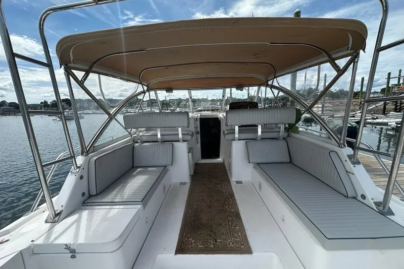 Slide: The Image of 2002 Mainship Pilot 34 boat interior with cushioned seating and canopy, docked by the water. - 9
