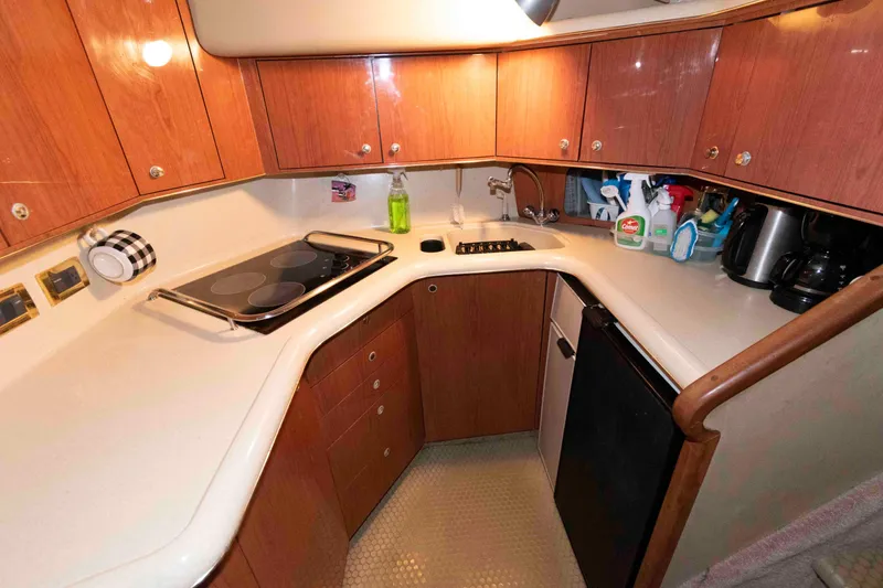 Slide: The Image of 1998 Sea Ray 370 Aft Cabin kitchen with wooden cabinets, stove, and cleaning supplies. - 16
