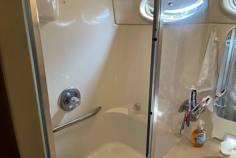 Slide: The Image of 1998 Sea Ray 370 Aft Cabin bathroom with shower, toiletries, and porthole window. - 23