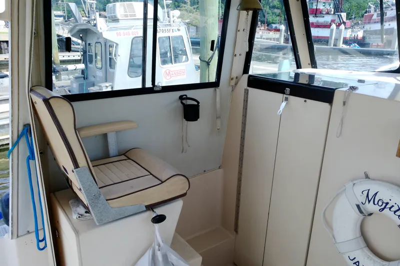 Slide: The Image of Interior of 2000 Atlas Boat Works Acadia 25, featuring seating and docked boats outside. - 20