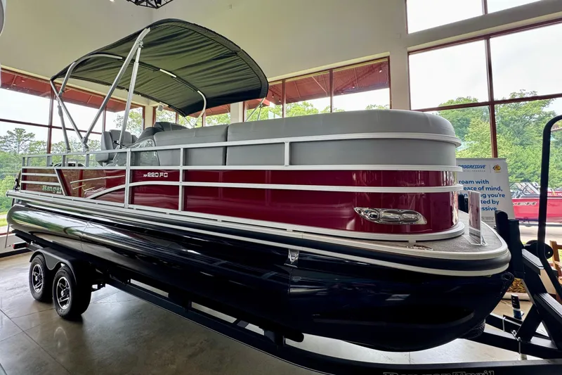 The Image of 2025 Ranger Reata 220FC pontoon boat displayed indoors with canopy and trailer. - 0
