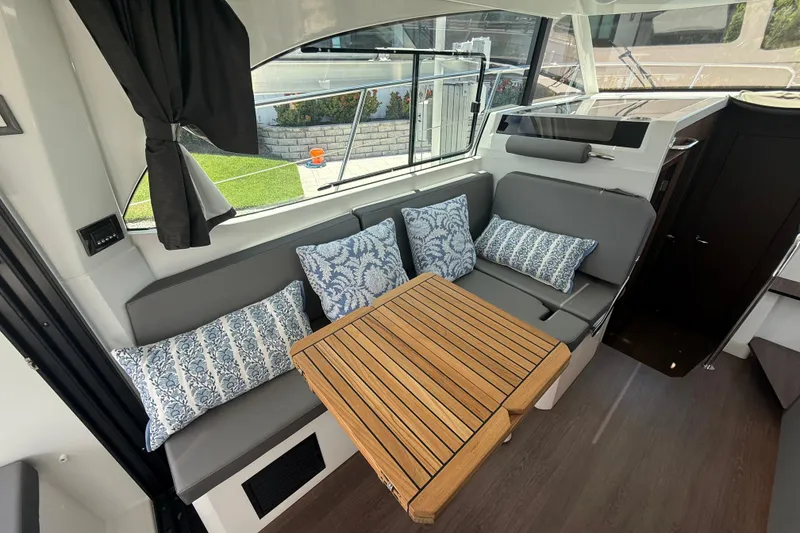Slide: The Image of 2024 Beneteau Antares 11 interior with cushioned seating and wooden table. - 16