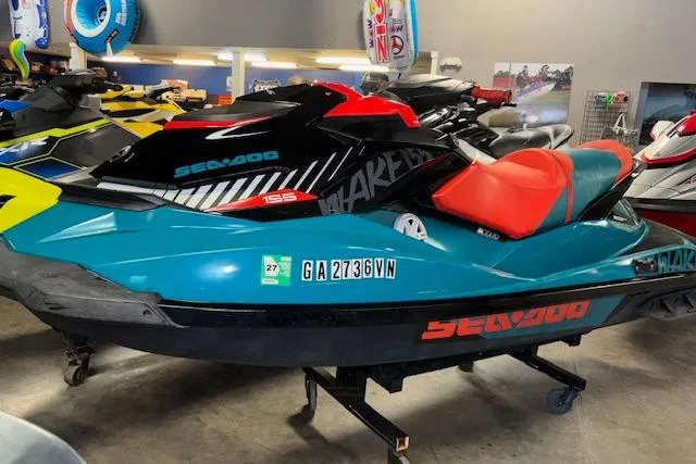 Slide: The Image of 2018 Sea-Doo Wake 155 jet ski in showroom, teal and red design. - 3