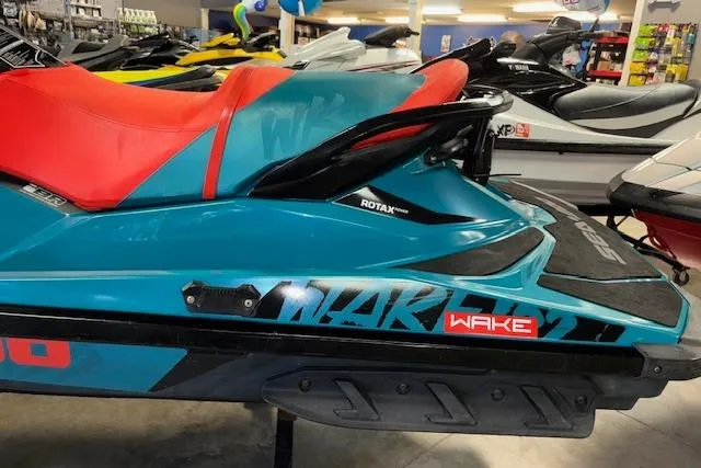 Slide: The Image of 2018 Sea-Doo Wake 155 jet ski with red seat and teal body in showroom. - 5