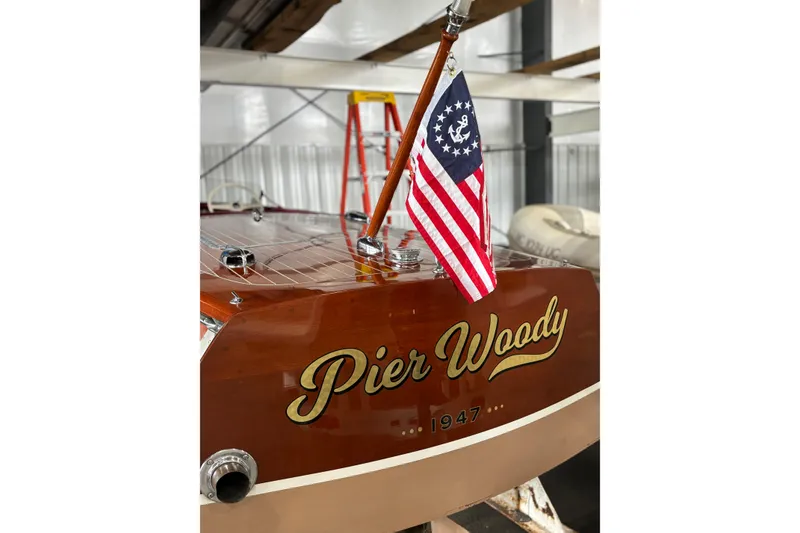 Slide: The Image of 1947 Chris-Craft Runabout boat with flag, named "Pier Woody," in a storage facility. - 2