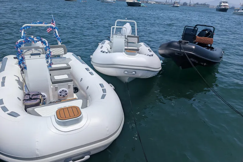 Slide: The Image of Three inflatable boats, including a 2026 Tide Craft Custom Black & Tan Catalina 13, anchored on water. - 2