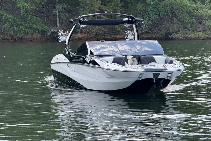 Slide: The Image of 2024 Centurion Fi23 boat cruising on a serene lake with lush green forest backdrop. - 2