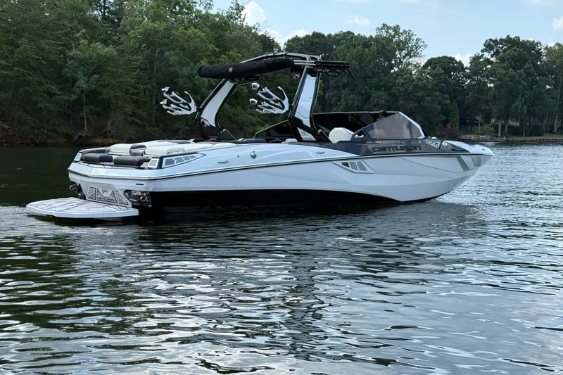 Slide: The Image of 2024 Centurion Fi23 boat on a calm lake with lush green trees. - 7