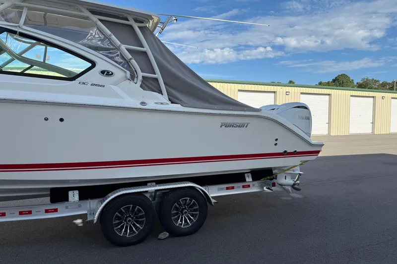 Slide: The Image of 2024 Pursuit DC 266 Dual Console boat on trailer, parked near storage units. - 47